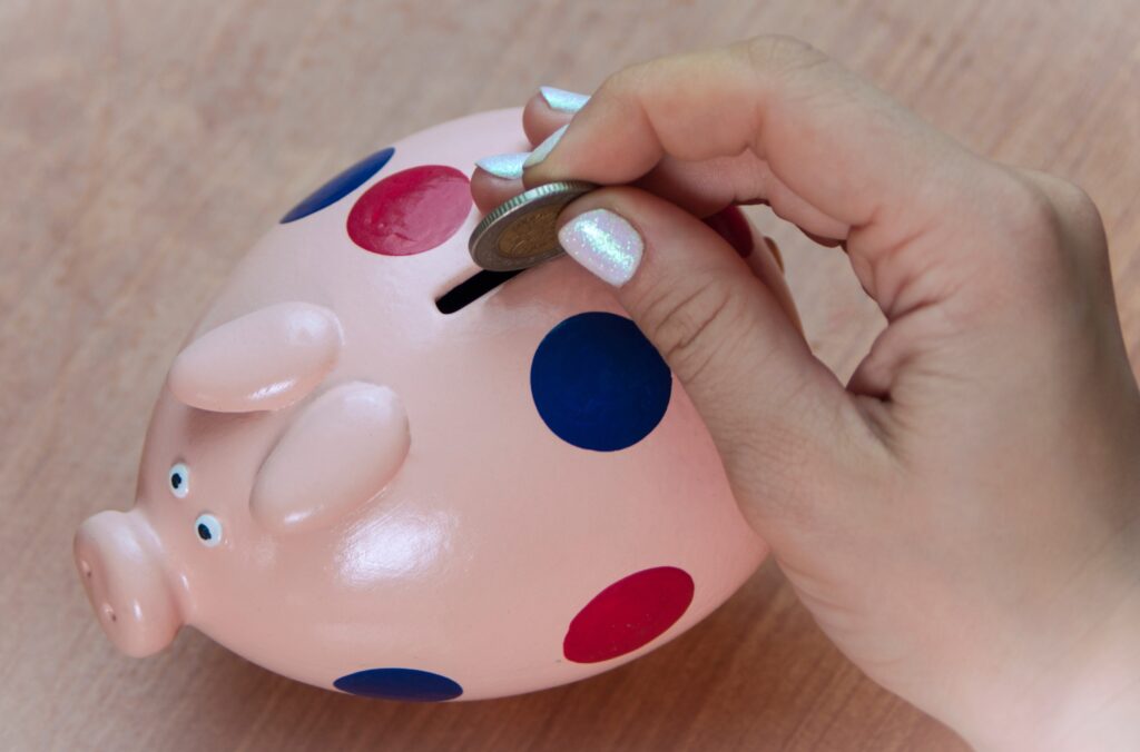 Photo of person dropping a coin in a piggy bank - This person is following step 4 of the Financial Oder of Operation - Saving for Emergencies